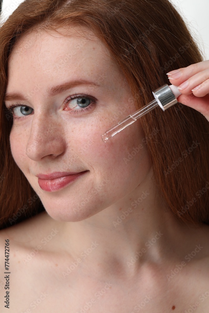 Beautiful woman with freckles applying cosmetic serum onto her face, closeup