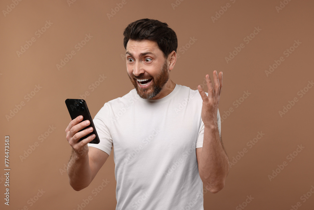 Happy man with smartphone on light brown background