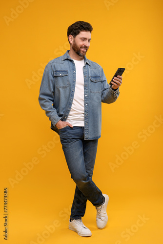 Photography Smiling man with smartphone on orange background