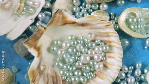 Oyster and scallop shells, sea pebbles and pearls on a blue background underwater. Ripples on the surface of clear water.