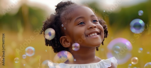 Cute African little girl having fun playing with soap bubbles at the park, holiday relaxation concept