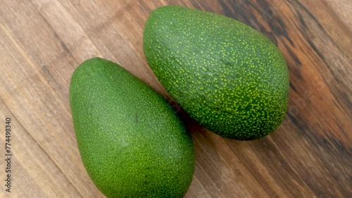 Close-up top view of Two Whole Avocado fruits rotating on a wooden surface.