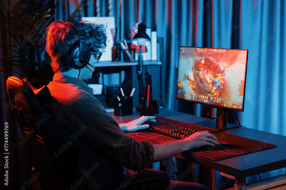Host channel of young gaming streamer playing fighting Moba at battle arena game with multiplays team, wearing headphone on pc monitor with back side image at neon digital light modern room. Gusher.