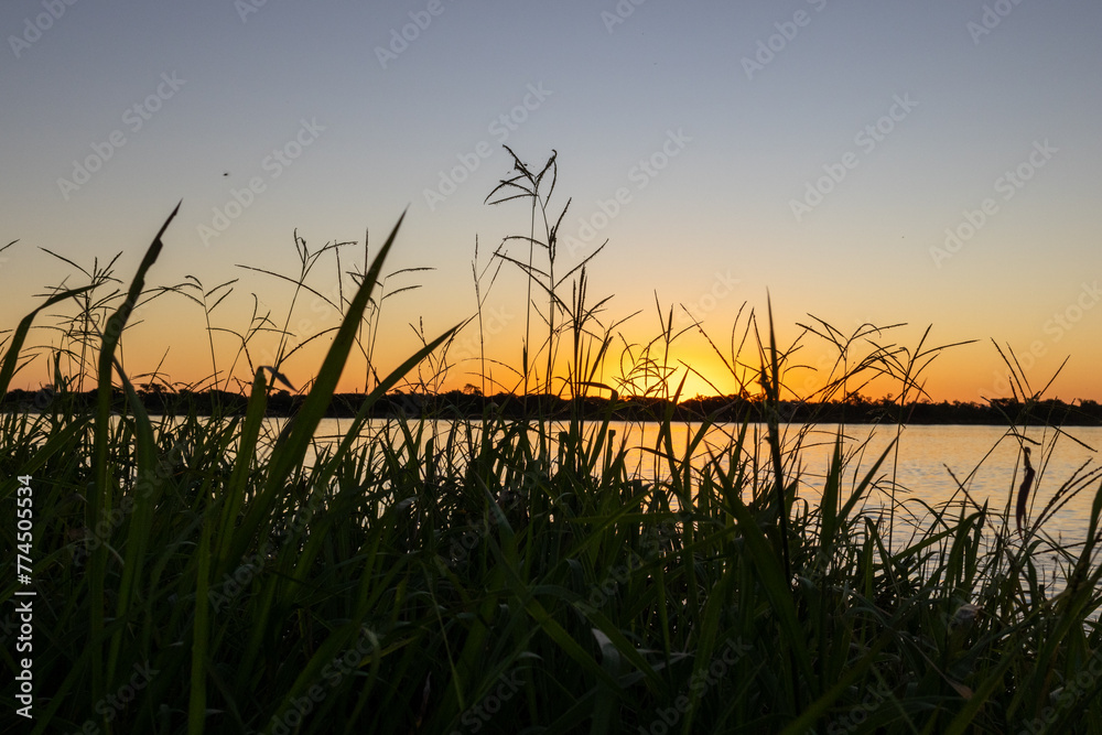 The sun hides behind the islands of the river Parana, View from the grasslands on the shore