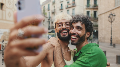 Gay couple stands hugging and makes video call from mobile phone, waving in greeting photo