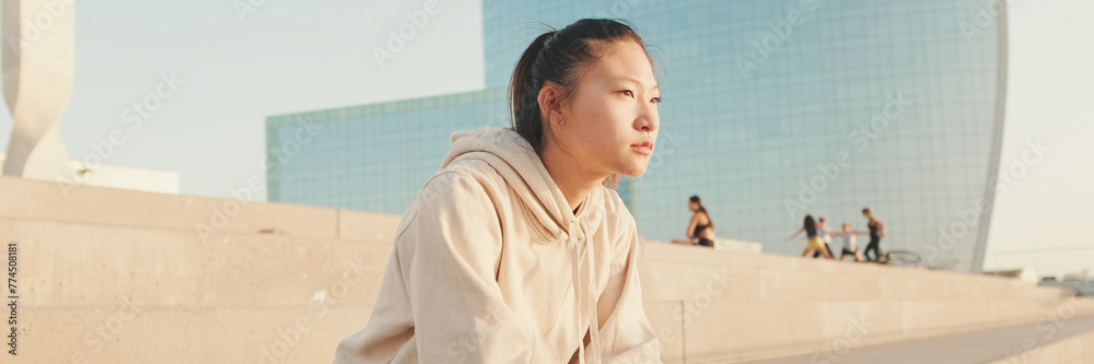 Asian girl in sportswear resting after workout sitting on steps on modern buildings background at sunrise, Panorama Asian girl in sportswear resting after workout sitting on steps on modern buildings background at sunrise, Panorama