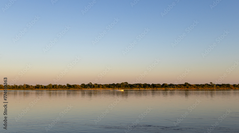 Panoramic photo of the sunrise on the Parana river. The islands and their vegetation are reflected in the calm water.