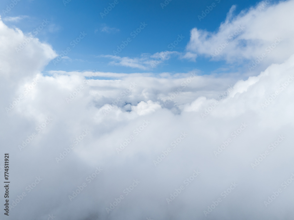 Obraz premium Aerial view of dense, white clouds covering Verbier, Switzerland, with a clear blue sky above, indicating high altitude and fair weather. Details of the town and landscape are obscured.