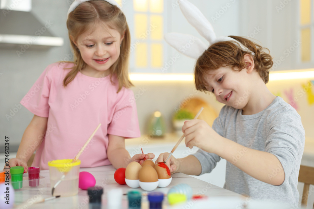 Easter celebration. Cute children with bunny ears painting eggs at white marble table in kitchen Easter celebration. Cute children with bunny ears painting eggs at white marble table in kitchen