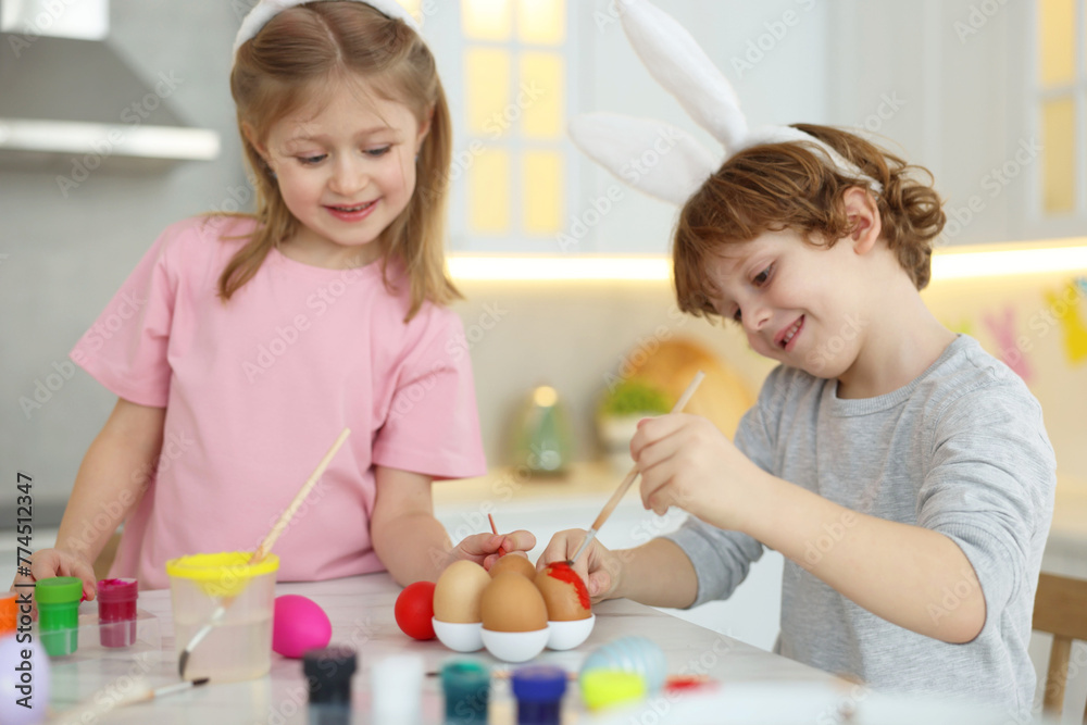 Easter celebration. Cute children with bunny ears painting eggs at white marble table in kitchen