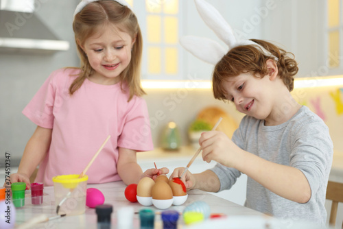 Easter celebration. Cute children with bunny ears painting eggs at white marble table in kitchen