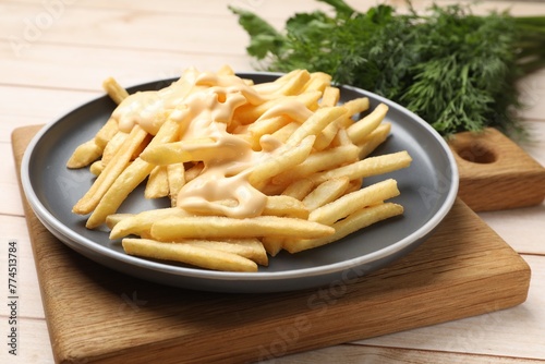 Delicious french fries with cheese sauce on wooden table, closeup