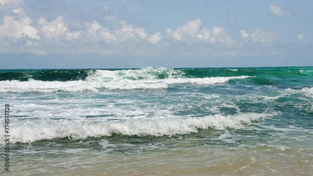 Waves crash onto sandy shore in a tropical setting with clear skies. Sunlight sparkles on turquoise ocean water. Pristine beach invites relaxation, water sports, nature appreciation. Slow motion.
