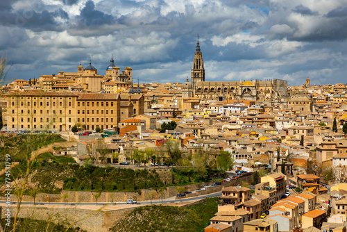 Scenic Toledo cityscape on hill above Tagus river with view of tall bell tower of medieval gothic Roman Catholic cathedral and domes of Church of San Ildefonso against cloudy sky in spring day, Spain photo