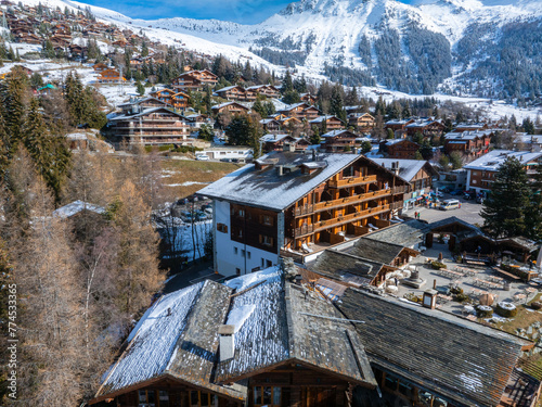Aerial shot of Verbier, Switzerland, shows chalet buildings with snow topped roofs in a mountain landscape, capturing the tranquility and beauty of winter in this ski resort town. photo
