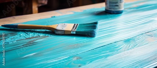 A close-up view of a paintbrush lying on a table freshly painted with blue color, showcasing the bristles and handle