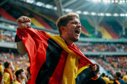 A man is holding a red, black, and yellow flag and is smiling. Football fan at the championship rejoices at a goal