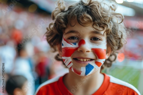 A young boy with a British flag painted on his face is smiling. Football fans at the football championship