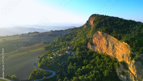 Wonderful aerial pullback and pan right shot from Montefalcone Appennino (Fermo) with a vision of hazy crests in the distance, rocky cliff with vegetation, old castle, buildings, badlands in the back photo