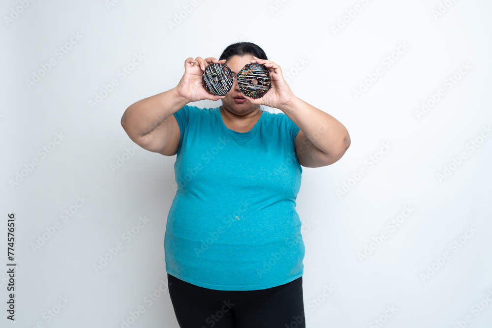 Overweight fat indian woman holding donuts in front of eyes and enjoying. isolated over white background. Plus size female. unhealthy eating. Copy Space