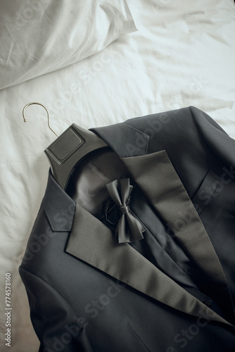 A sophisticated dark suit with a bow tie, neatly arranged on a white bed photo