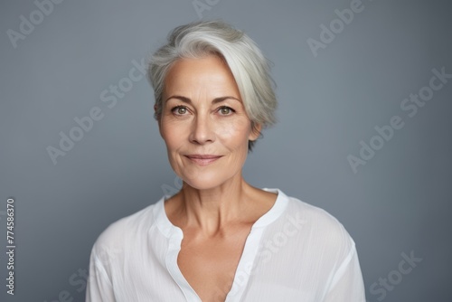 Portrait of beautiful mature woman looking at camera and smiling while standing against grey background