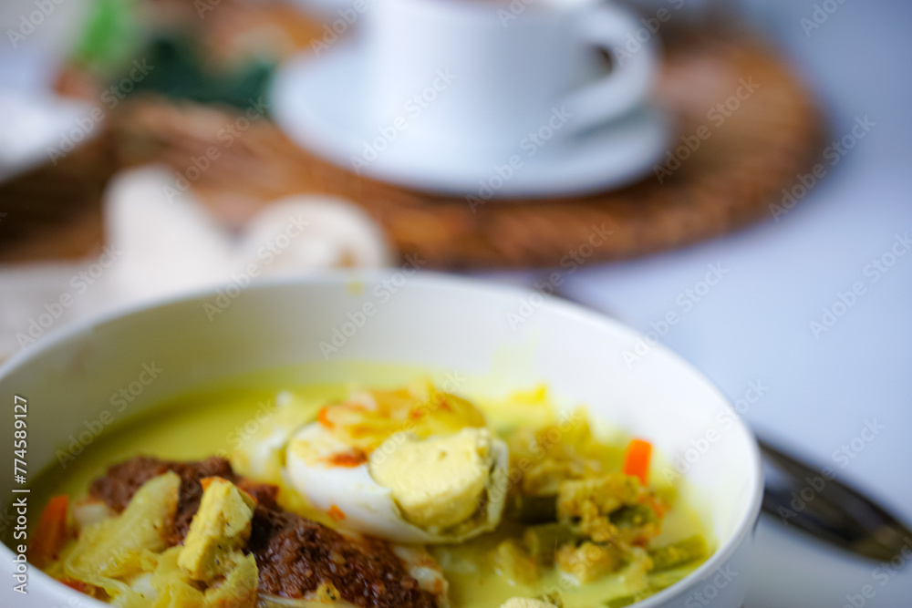A bowl of “Lontong” or rice cake and coconut gravy with tumeric, chilli, and vegetables with some shadow and selective focus.