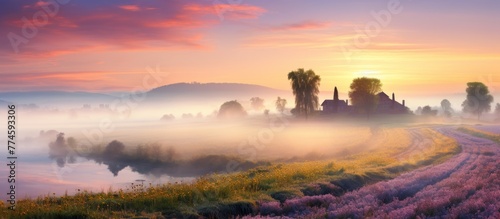 Morning mist covers the serene landscape with a flowing river, open field, and a picturesque church in the distance