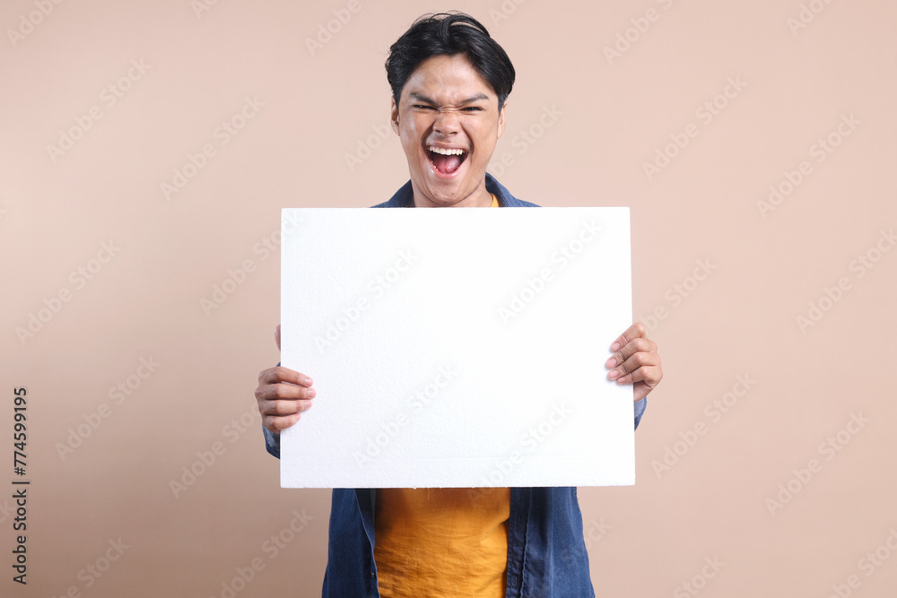 Excited young man holding white blank board for text or ads with happy expression Excited young man holding white blank board for text or ads with happy expression