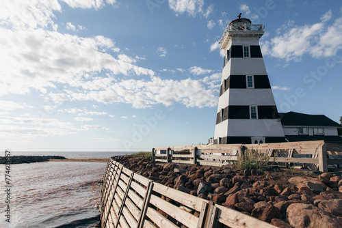 vue sur un phare ligné noir et blanc en bord de mer avec une clôture en bois en avant plan
