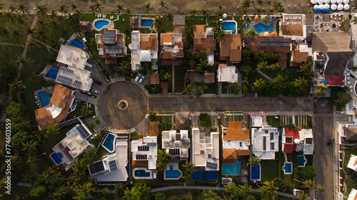 vista aérea de casas de playa junto a la arena y el mar con sombrillas playeras techos de casas con alberca casas sobre la avenida con glorieta llena de árboles en la costa photo