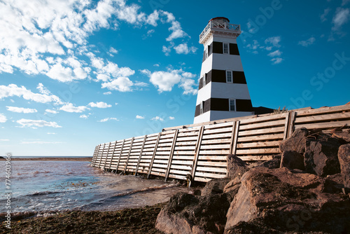vue en bas angle sur un phare ligné noir et blanc en bord de mer avec un brise-vague en bois et des roches en avant plan photo