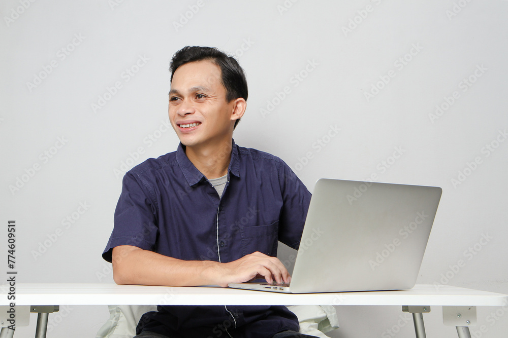 joyfull happy asian man at workplace while sitting in front of laptop computer. on isolated background joyfull happy asian man at workplace while sitting in front of laptop computer. on isolated background