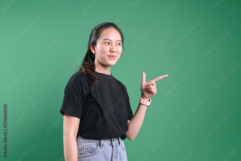 Portrait of beautiful young woman pointing to the side over green background.
