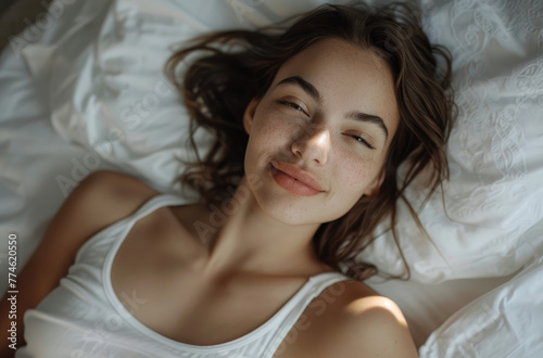 A beautiful woman sleeping on her side with white sheets and pillow, she is smiling in dreamy background