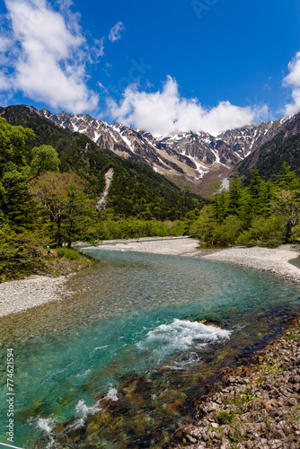 Clear, fast flowing mountain river in a forested valley in front of snowy peaks