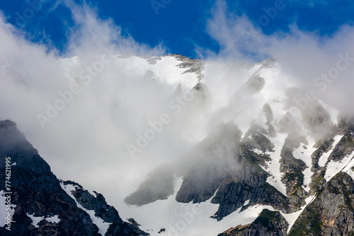 Clouds over the top of tall, jagged, snow covered mountain peaks
