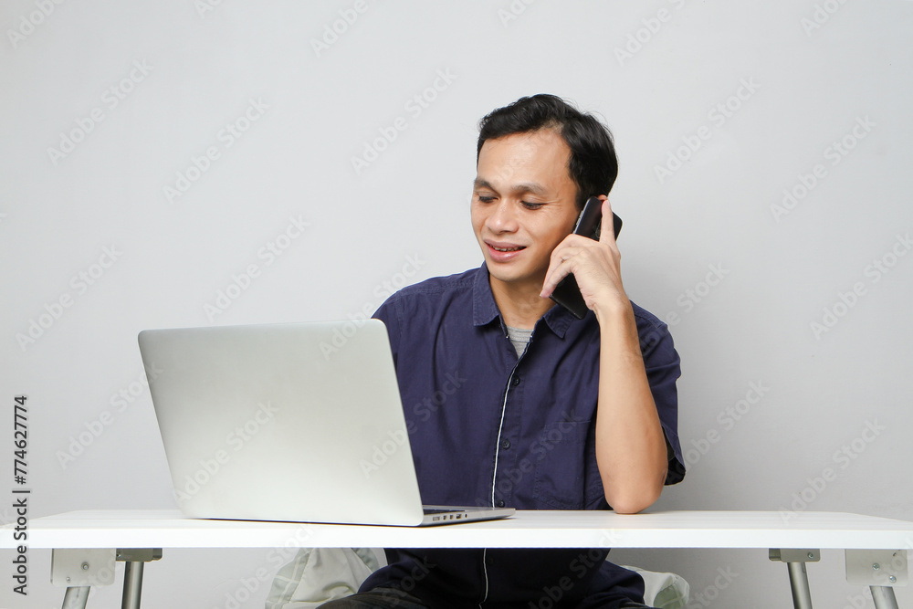 joyfull happy asian man make a phone call while sitting in front of laptop computer. on isolated background joyfull happy asian man make a phone call while sitting in front of laptop computer. on isolated background