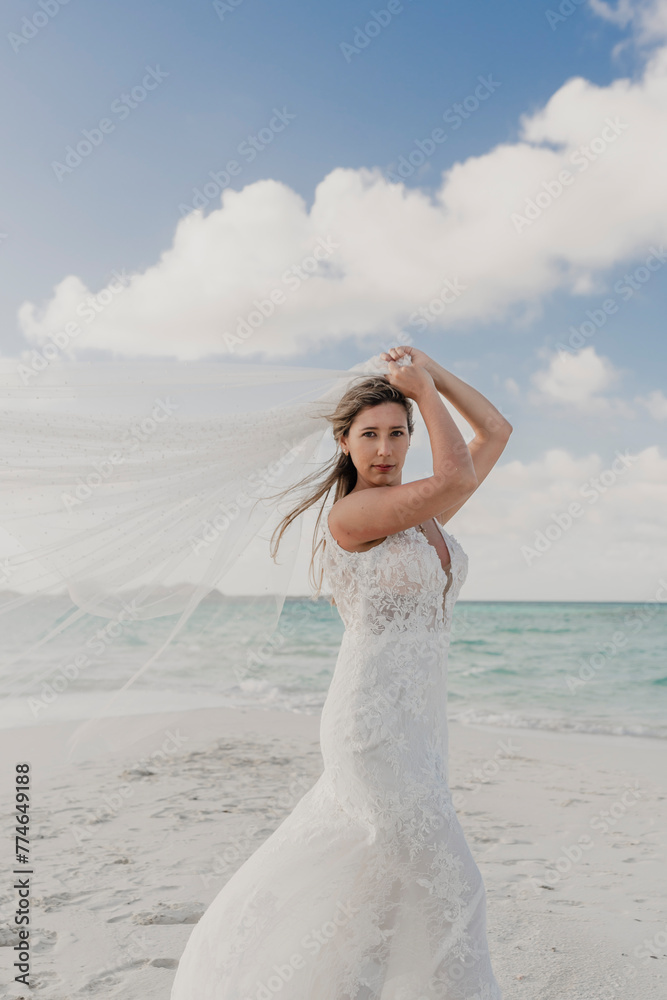 beautiful bride on the beach sand playing with her veil in the wind beautiful bride on the beach sand playing with her veil in the wind