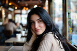 Portreit of a young beautiful girl with long black hair sits at a table in a cafe enjoying of hot coffee