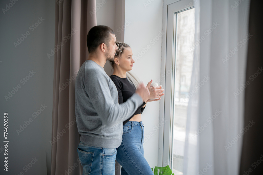 Man and Woman Standing by Window looking outside, drinking hot tea together Man and Woman Standing by Window looking outside, drinking hot tea together