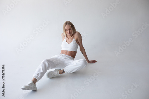 Beautiful blonde girl in a white top and tights posing on a white background