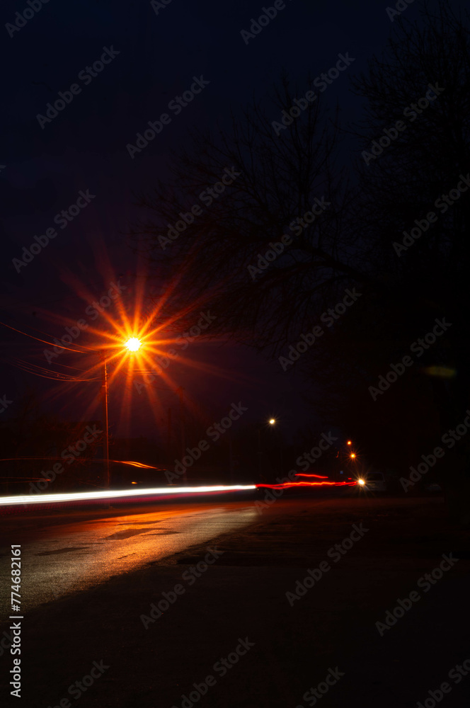 Night falls on a quiet street, its tranquility captured in the dance of light and shadow, illuminated by passing cars.
