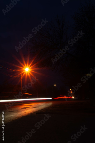 Night falls on a quiet street, its tranquility captured in the dance of light and shadow, illuminated by passing cars. 