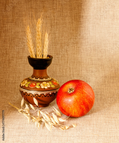 Still life with an apple, a clay jug with ears of wheat, against a background of natural linen.