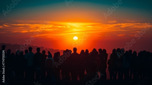 A group of people are standing on a hillside and watching the sun set. The sky is filled with clouds and the sun is setting in the distance