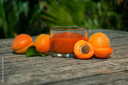 Apricot jam and ripe apricots on a wooden table. Glass jar of apricot jam with ripe apricots on an old rustic wooden table in a garden. Glass jar of apricot jam on summer shiny day.