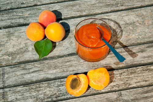Apricot jam and ripe apricots on a wooden table. Glass jar of apricot jam with ripe apricots on an old rustic wooden table in a garden. Glass jar of apricot jam on summer shiny day.