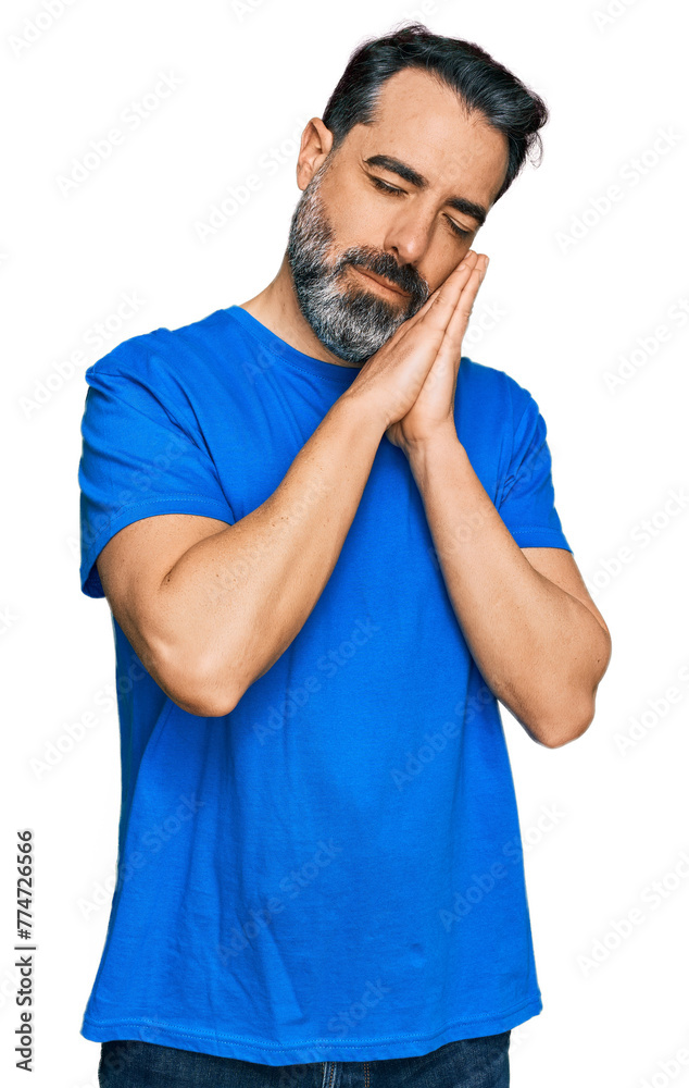 Middle aged man with beard wearing casual blue t shirt sleeping tired dreaming and posing with hands together while smiling with closed eyes. Middle aged man with beard wearing casual blue t shirt sleeping tired dreaming and posing with hands together while smiling with closed eyes.