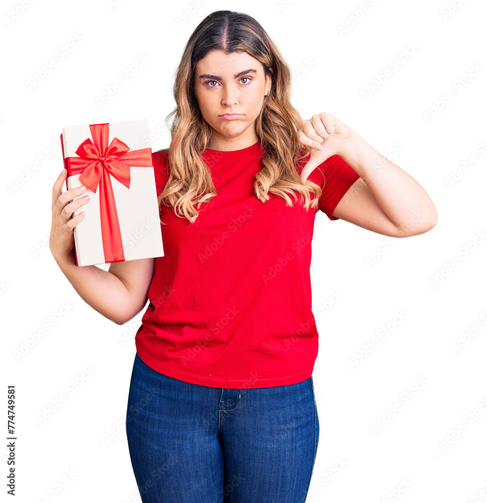 Young caucasian woman holding gift with angry face, negative sign showing dislike with thumbs down, rejection concept